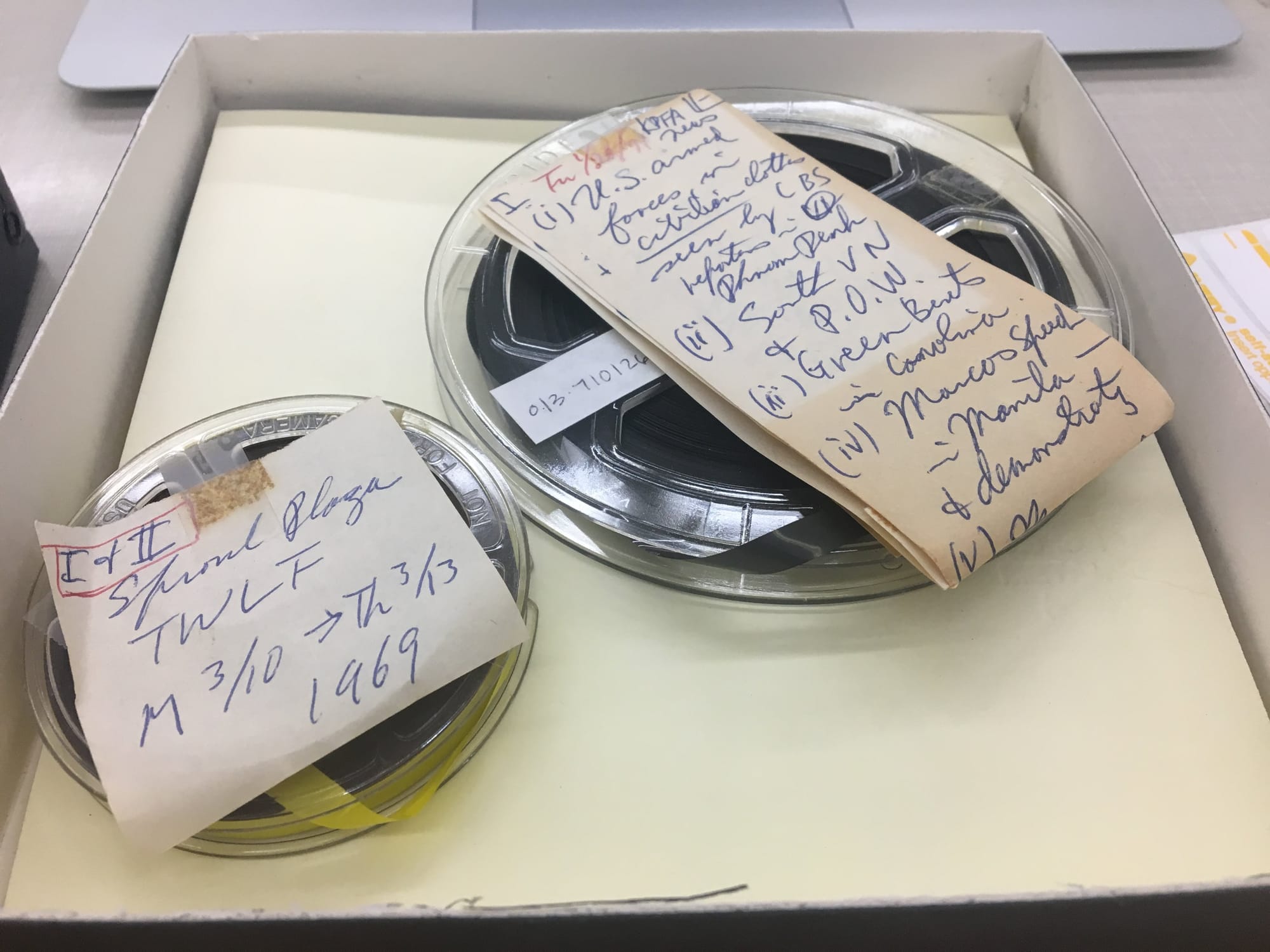 Two circular reels are placed next to each other with handwritten labels taped on top of them in dark blue ink. They are placed next to each other in a white box.